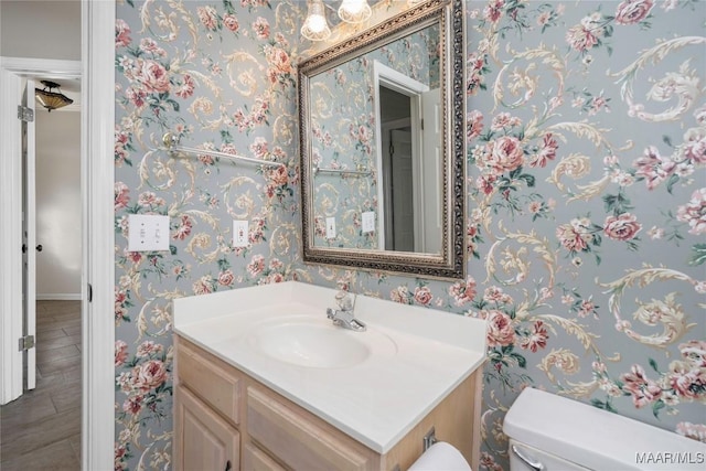 half bath with vanity, toilet, and wallpapered walls