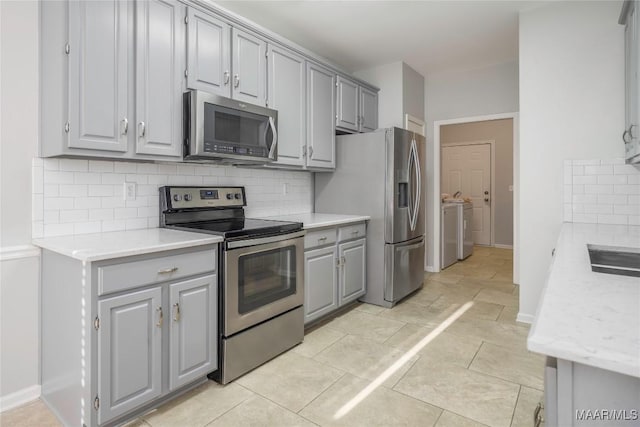 kitchen with stainless steel appliances, light countertops, gray cabinets, backsplash, and washing machine and clothes dryer