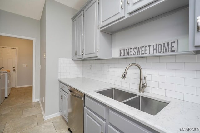 kitchen featuring washer and clothes dryer, backsplash, gray cabinetry, stainless steel dishwasher, and a sink