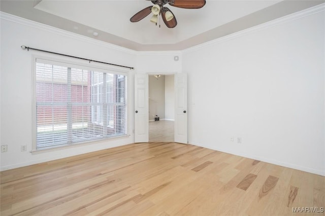 spare room with baseboards, a ceiling fan, wood finished floors, a tray ceiling, and crown molding