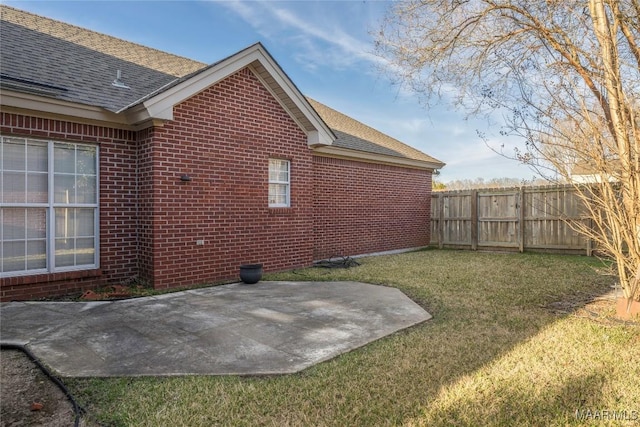 exterior space featuring brick siding, a patio, a shingled roof, a lawn, and fence