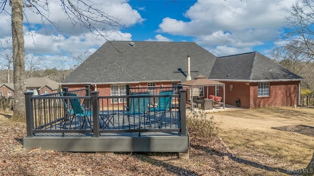 rear view of property featuring brick siding, a deck, a gazebo, and roof with shingles