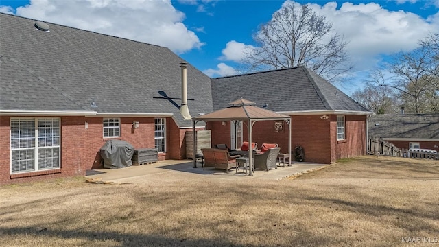 rear view of property featuring brick siding, a shingled roof, a gazebo, a lawn, and a patio area