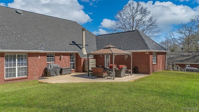 rear view of house featuring a shingled roof, a lawn, a gazebo, a patio area, and brick siding