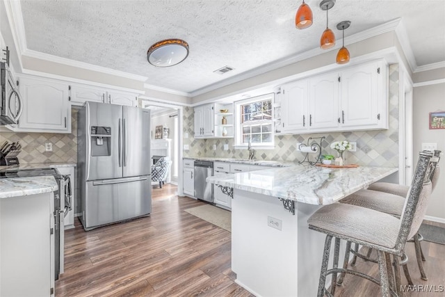 kitchen with dark wood-style flooring, appliances with stainless steel finishes, white cabinets, light stone countertops, and a peninsula