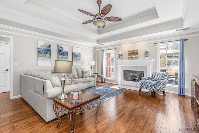 living room featuring a tray ceiling, visible vents, hardwood / wood-style floors, and a tile fireplace