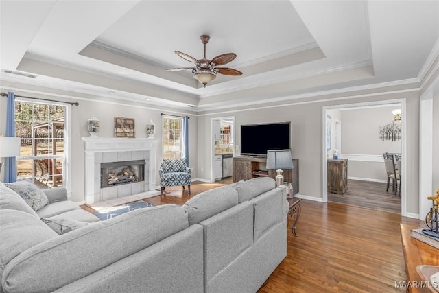 living room with a tray ceiling, visible vents, a tiled fireplace, and wood finished floors