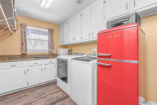 clothes washing area with a sink, visible vents, wood finished floors, washer and dryer, and cabinet space