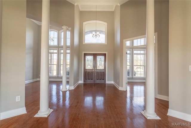 foyer with wood finished floors, a towering ceiling, and ornate columns