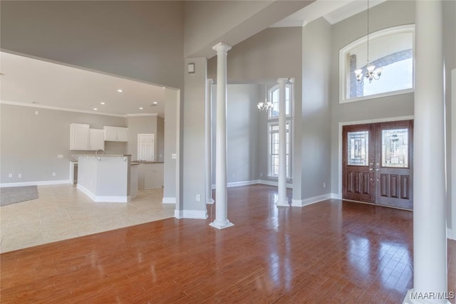 entryway featuring a high ceiling, french doors, light wood-type flooring, ornate columns, and a chandelier