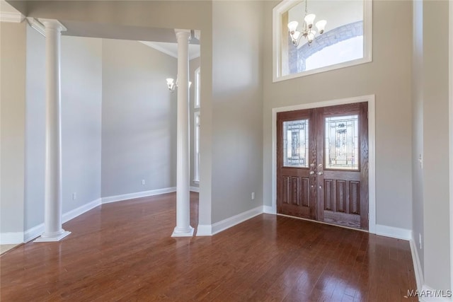 foyer entrance with decorative columns, baseboards, a towering ceiling, hardwood / wood-style floors, and a notable chandelier