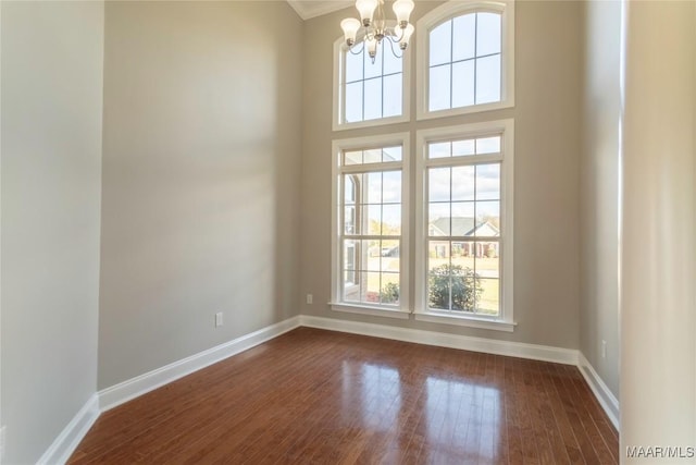 unfurnished room with baseboards, a chandelier, and dark wood finished floors