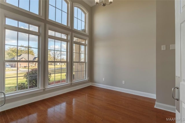 spare room with dark wood-type flooring, a towering ceiling, baseboards, and an inviting chandelier