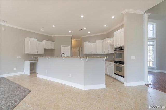 kitchen featuring double oven, decorative columns, white cabinetry, and baseboards