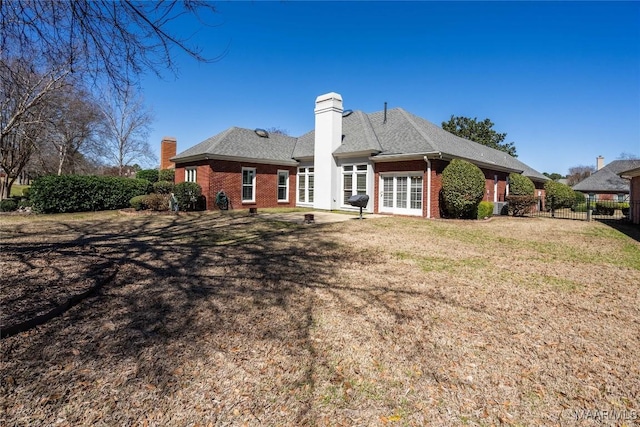 back of house featuring french doors, brick siding, a chimney, a lawn, and fence