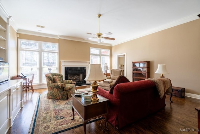 living area with dark wood-style floors, crown molding, visible vents, a ceiling fan, and a tile fireplace
