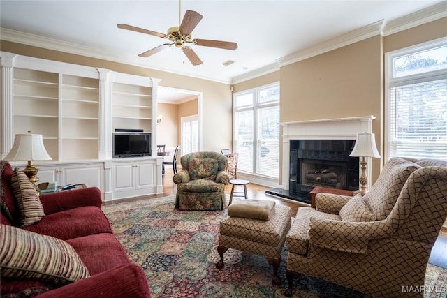 living room featuring ornamental molding, ceiling fan, a tiled fireplace, and wood finished floors