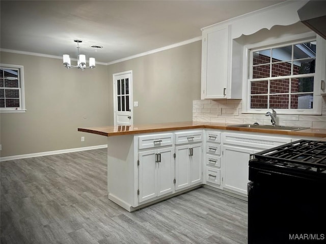 kitchen featuring black gas range, tasteful backsplash, a peninsula, crown molding, and a sink