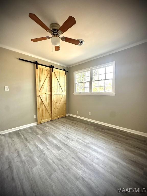 spare room featuring a barn door, ornamental molding, ceiling fan, wood finished floors, and baseboards