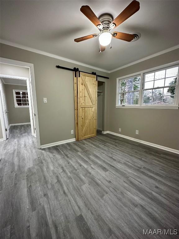 unfurnished bedroom with a barn door, baseboards, dark wood-type flooring, and crown molding