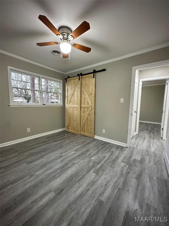 unfurnished bedroom with a barn door, visible vents, baseboards, dark wood-style flooring, and crown molding