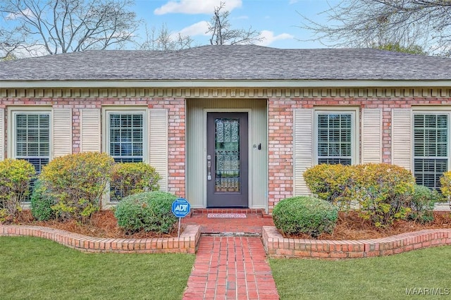 entrance to property featuring a shingled roof and brick siding