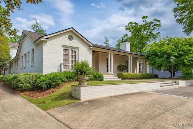 single story home featuring covered porch, a chimney, and brick siding