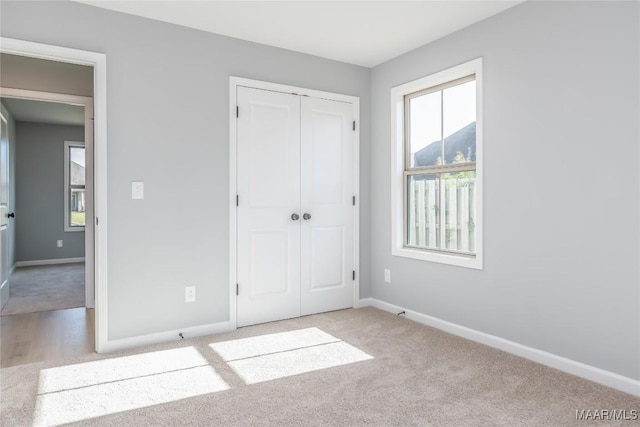 unfurnished bedroom with a closet, light carpet, and baseboards