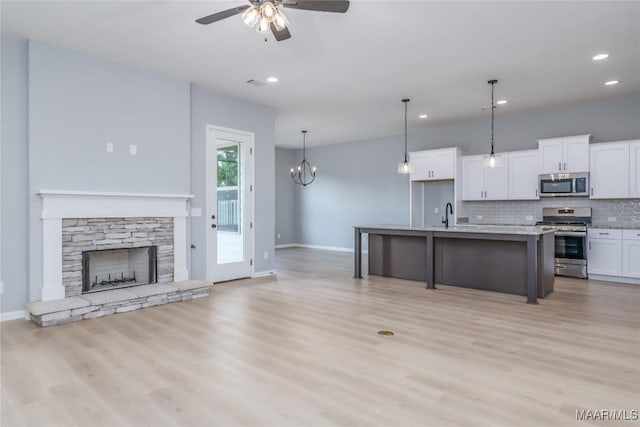 kitchen featuring a stone fireplace, ceiling fan with notable chandelier, stainless steel appliances, white cabinets, and decorative backsplash