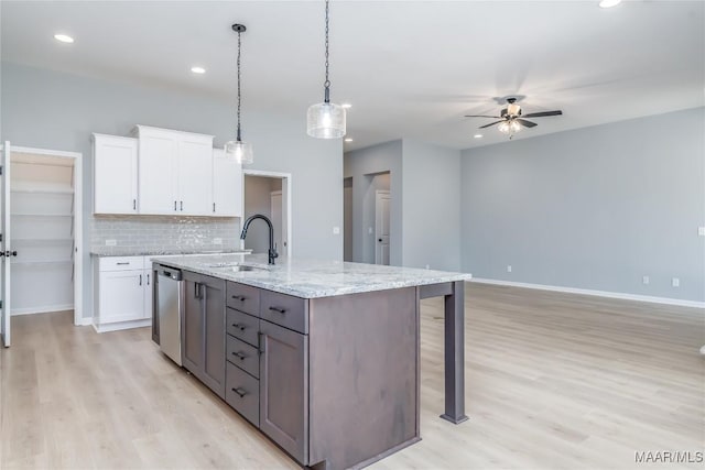 kitchen with stainless steel dishwasher, an island with sink, a sink, and white cabinets