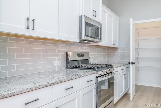 kitchen featuring stainless steel appliances, white cabinets, light wood-type flooring, light stone countertops, and tasteful backsplash