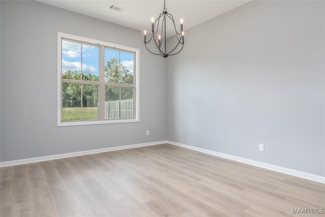 spare room with a chandelier, visible vents, baseboards, and wood finished floors