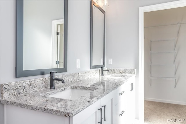 bathroom featuring double vanity, a sink, a walk in closet, and baseboards