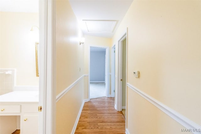 corridor featuring attic access, light wood-style flooring, and baseboards