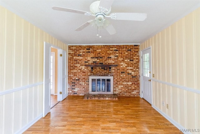 unfurnished living room with ceiling fan, a fireplace, ornamental molding, and wood finished floors