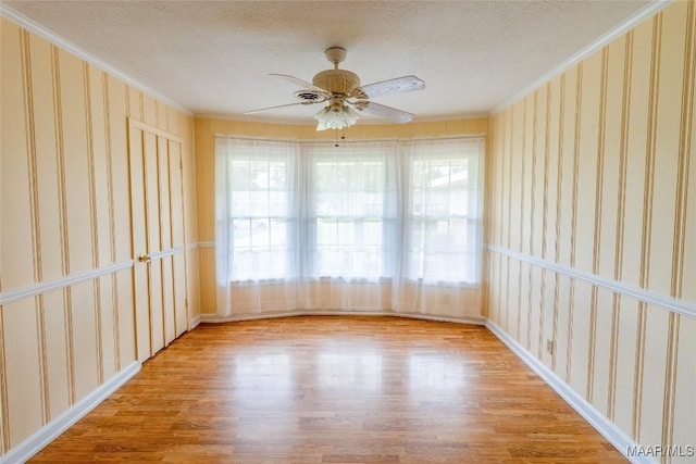 spare room with wallpapered walls, a textured ceiling, crown molding, and wood finished floors