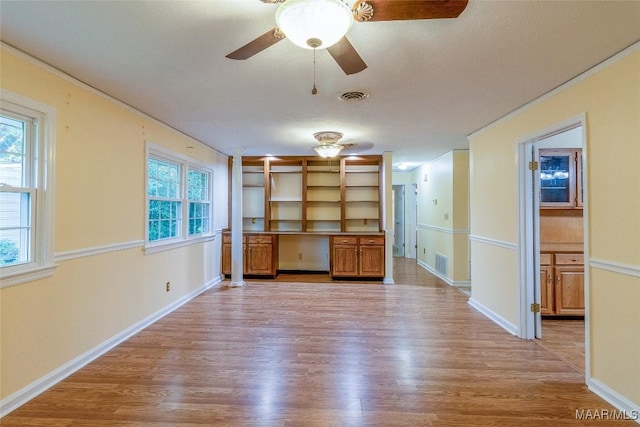 empty room featuring built in desk, light wood-type flooring, and visible vents