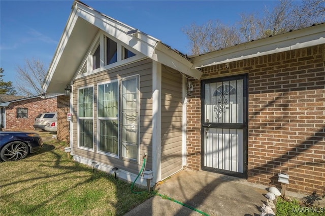 doorway to property with brick siding and a lawn