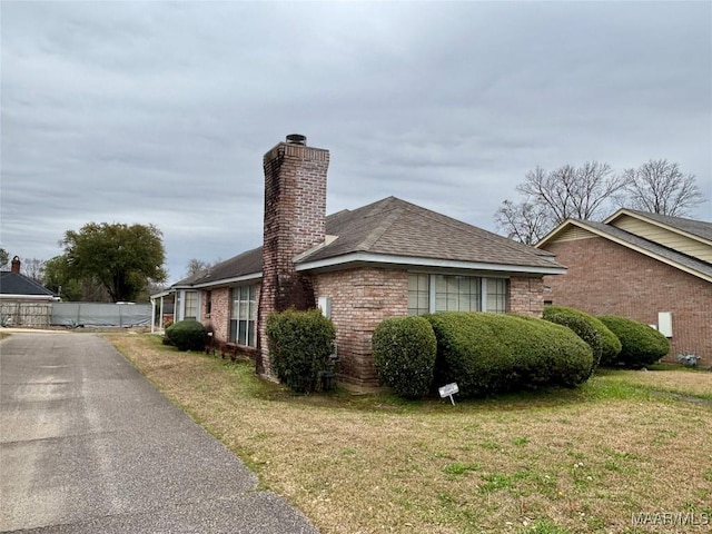 view of side of property with brick siding, a lawn, and a chimney