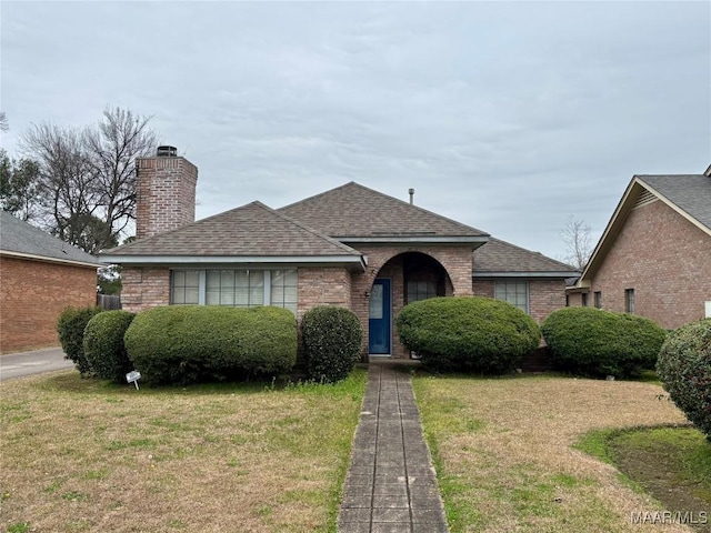 view of front of property featuring a shingled roof, a chimney, a front yard, and brick siding