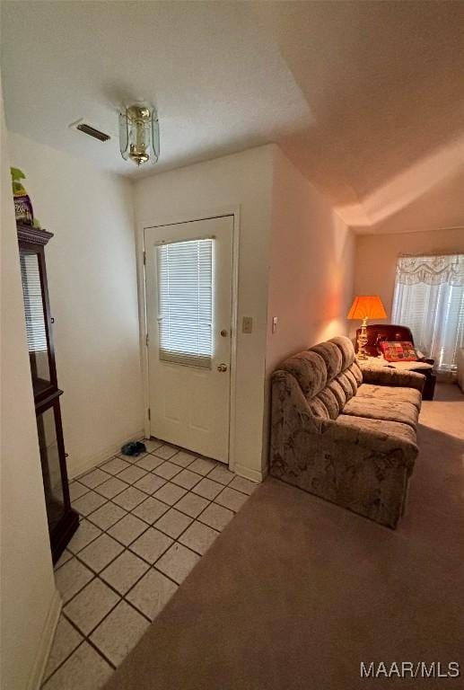 entryway featuring light tile patterned floors, visible vents, vaulted ceiling, and light colored carpet