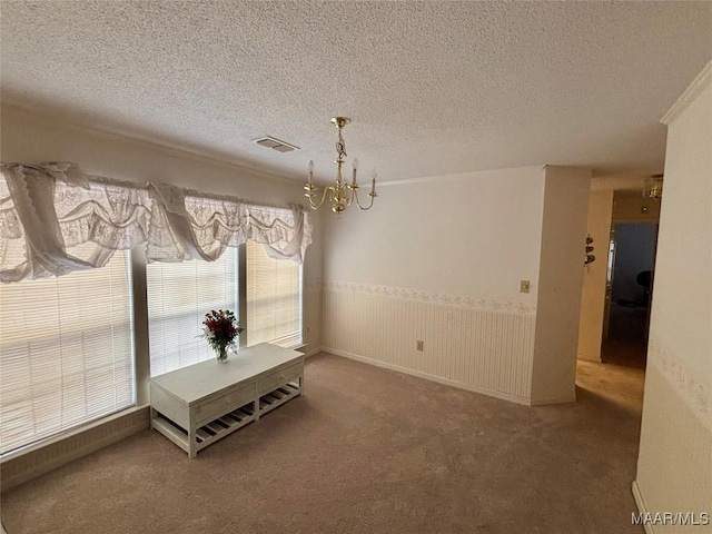 unfurnished dining area featuring carpet floors, a wainscoted wall, visible vents, and a textured ceiling