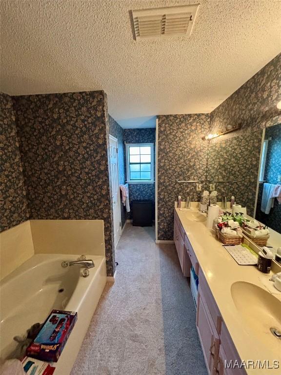 ensuite bathroom featuring a textured ceiling, a sink, visible vents, ensuite bath, and wallpapered walls