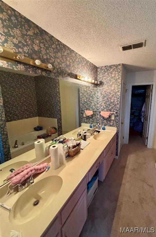 bathroom featuring wallpapered walls, a textured ceiling, visible vents, and a sink