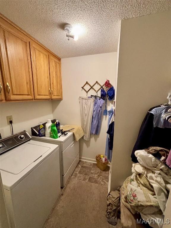 clothes washing area featuring washing machine and dryer, cabinet space, a textured ceiling, and baseboards