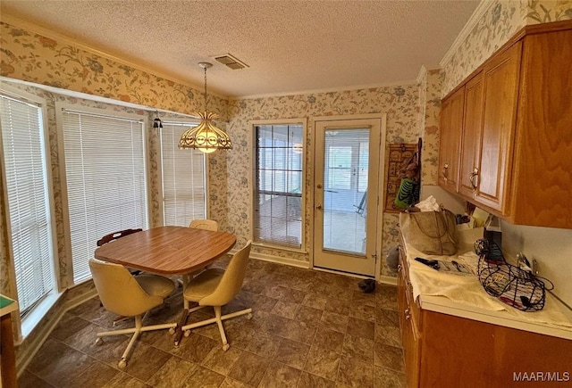 dining space with a textured ceiling, ornamental molding, visible vents, and wallpapered walls