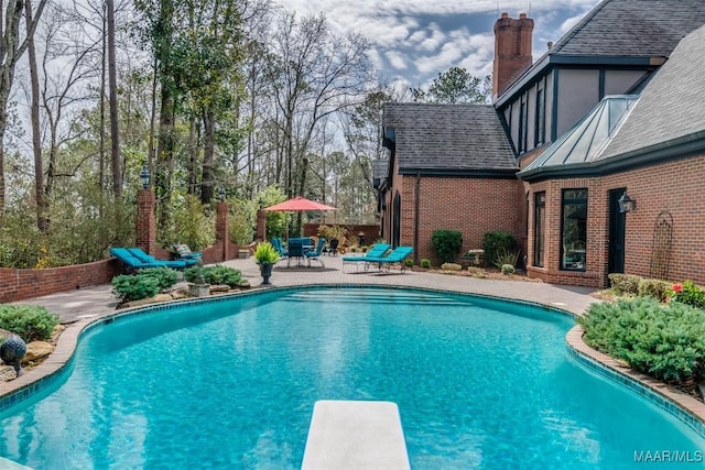 outdoor pool featuring a diving board and a patio