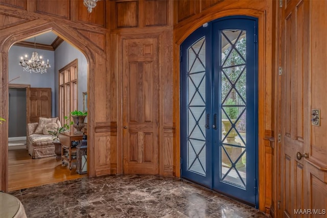 foyer entrance featuring arched walkways, a chandelier, french doors, and ornamental molding