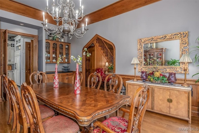 dining space with arched walkways, a wainscoted wall, light wood-style floors, beam ceiling, and an inviting chandelier