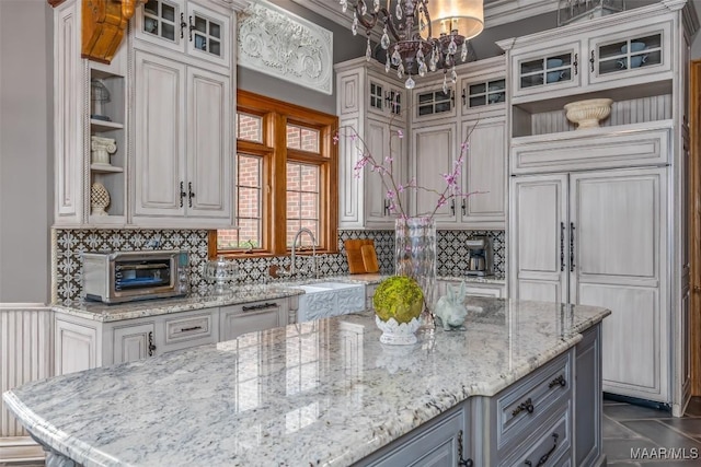 kitchen featuring light stone counters, a toaster, a sink, decorative backsplash, and open shelves